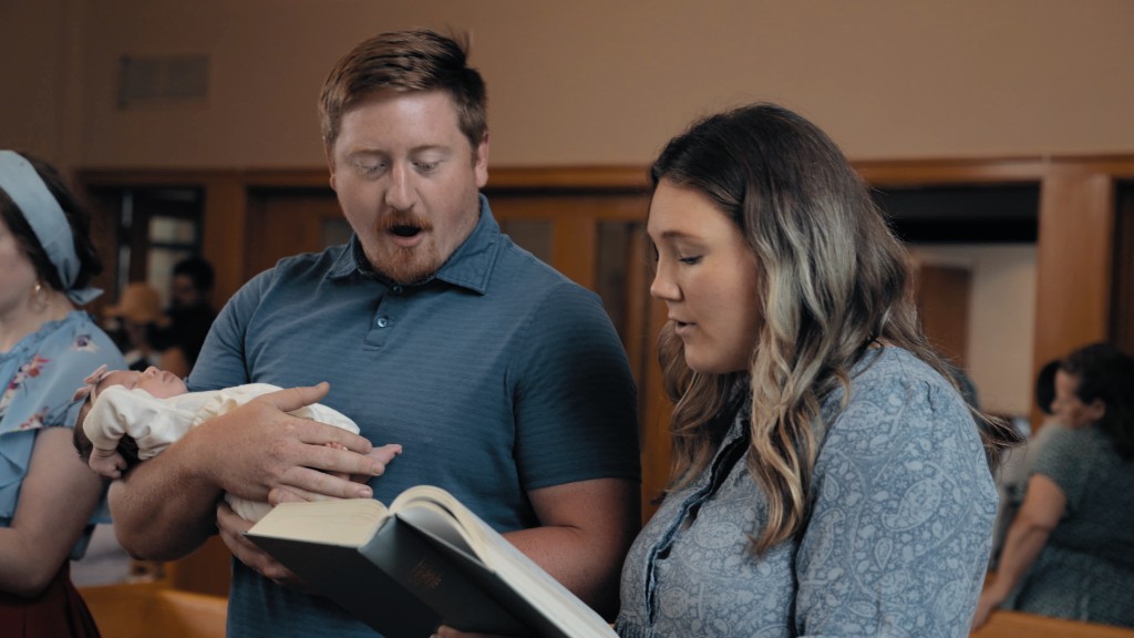 A father holding his newborn while his wife sings from a psalter