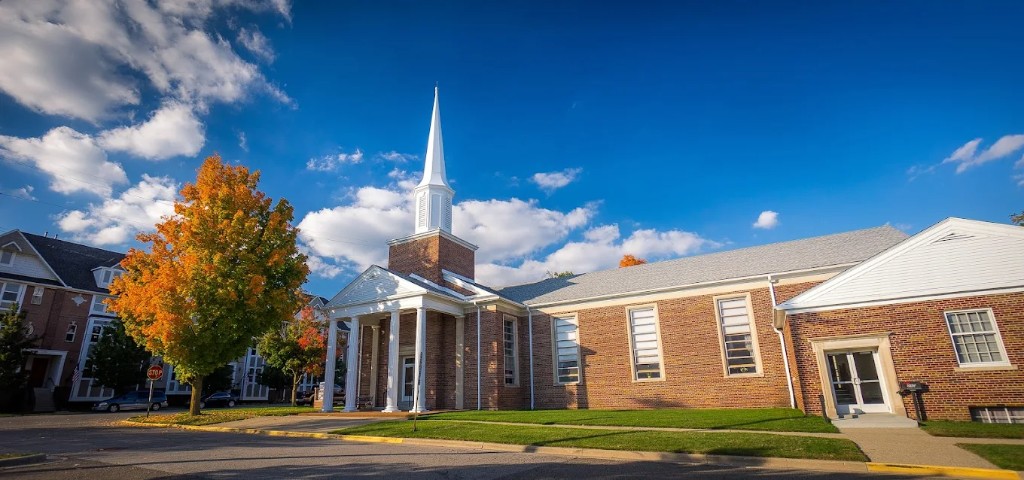 Christ Church of Livingston County: red brick exterior with white columns, steeple, and autumn trees in Howell, Michigan